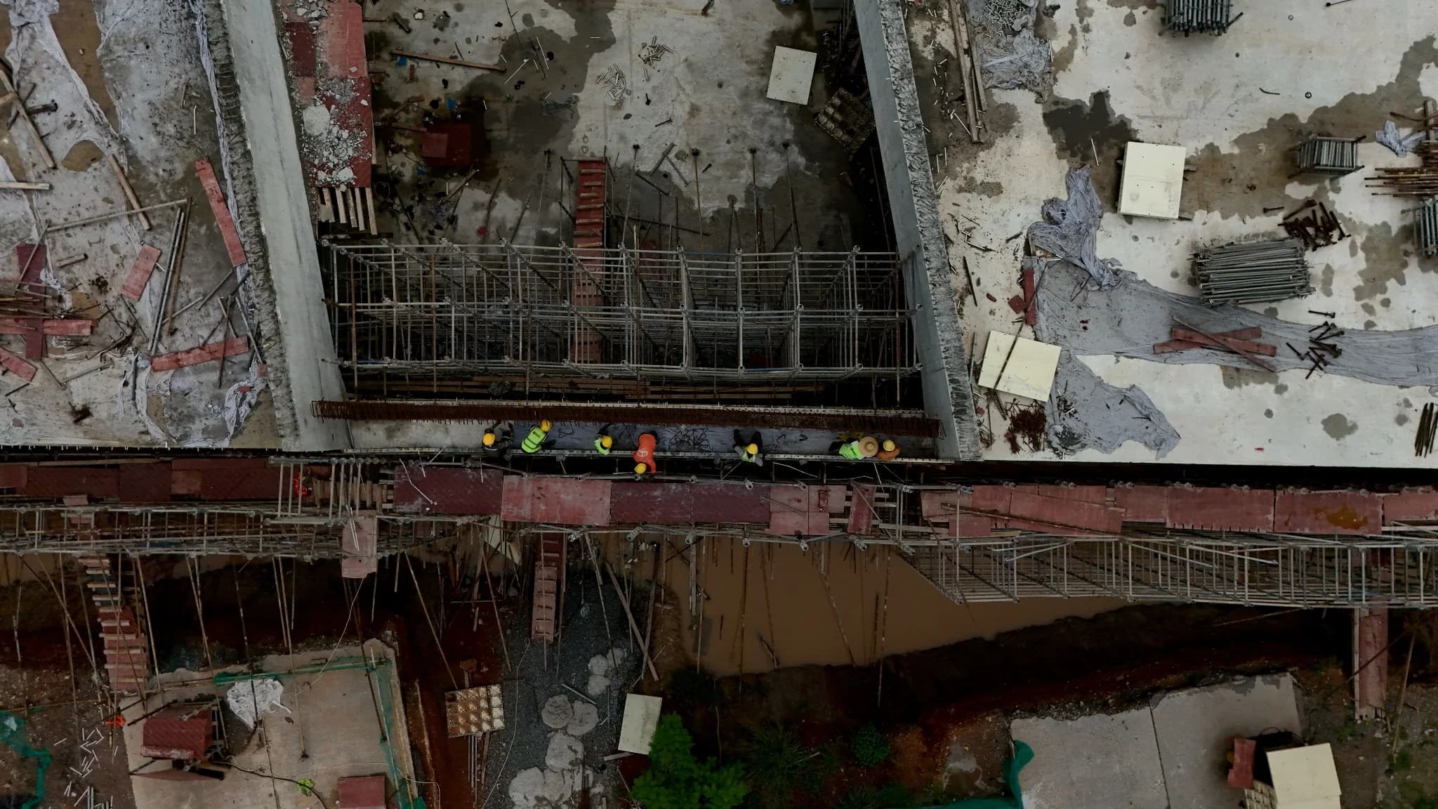 Overhead aerial view of a bridge deck under construction, showing the deck reinforcement steel and workers in high-visibility gear on the span