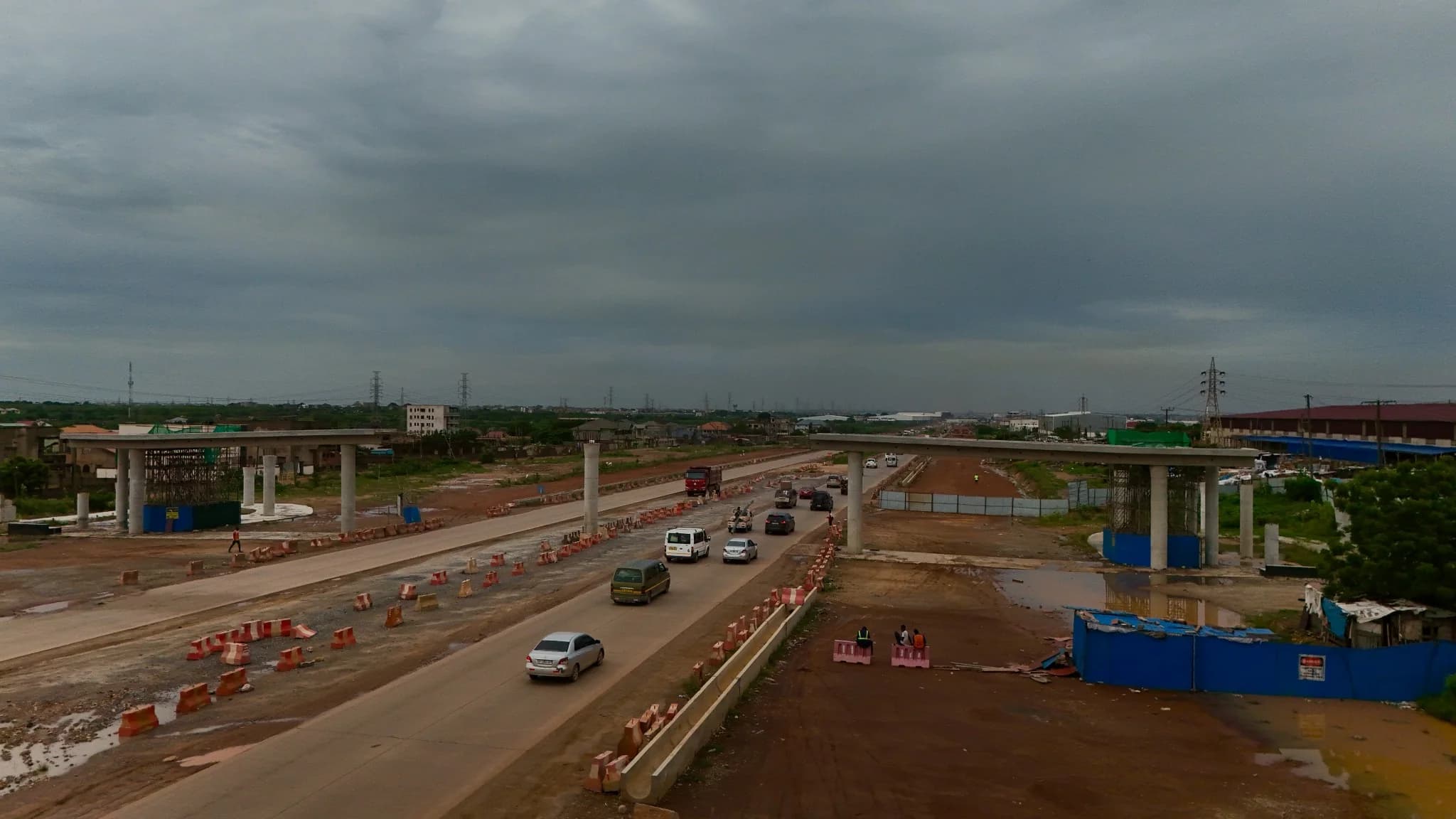 Aerial view of completed overpass piers and crossheads straddling the corridor at dusk, with traffic on the road below