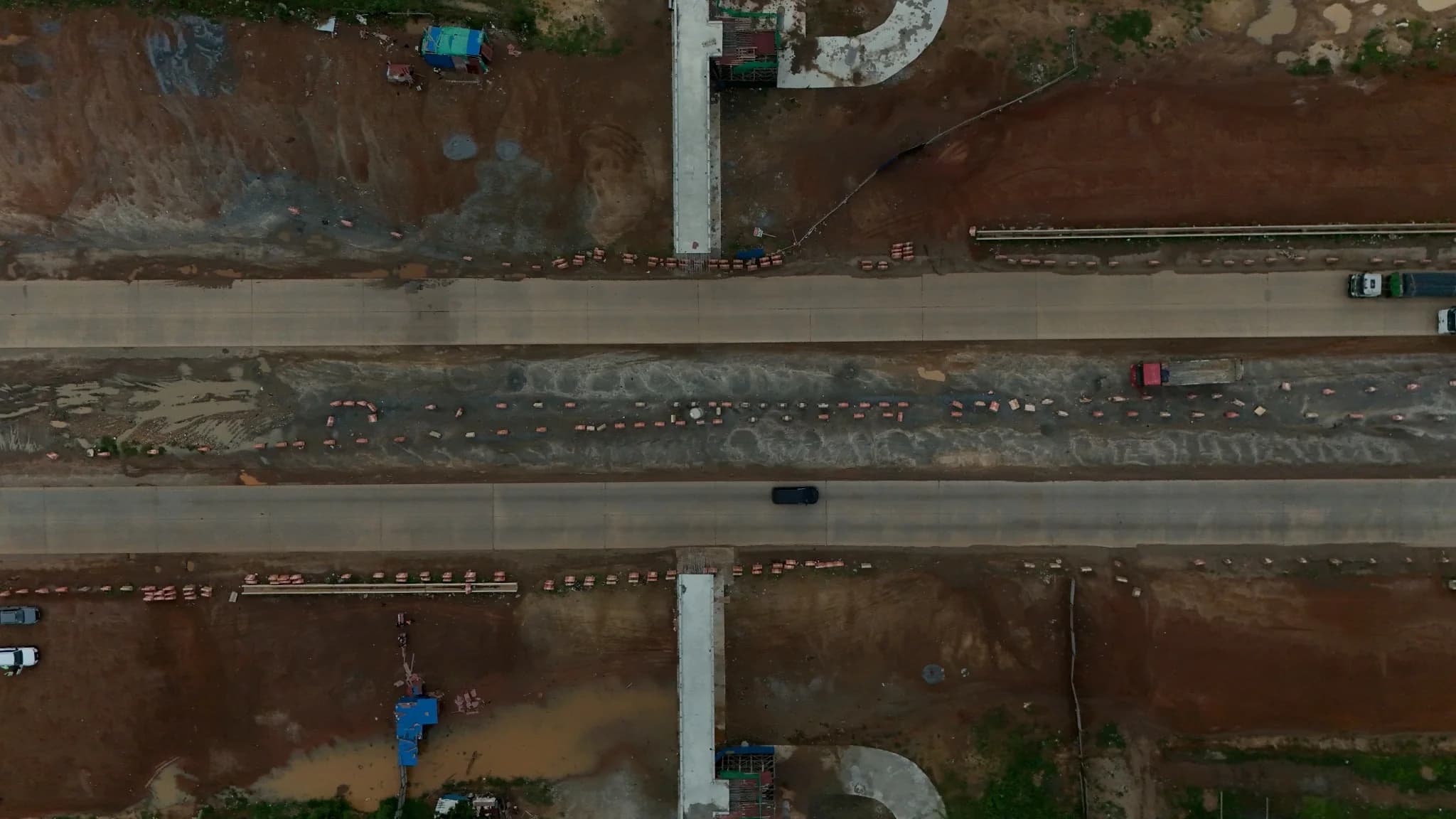 Overhead aerial view of a completed concrete carriageway section with roadside ramp structures under construction on both sides