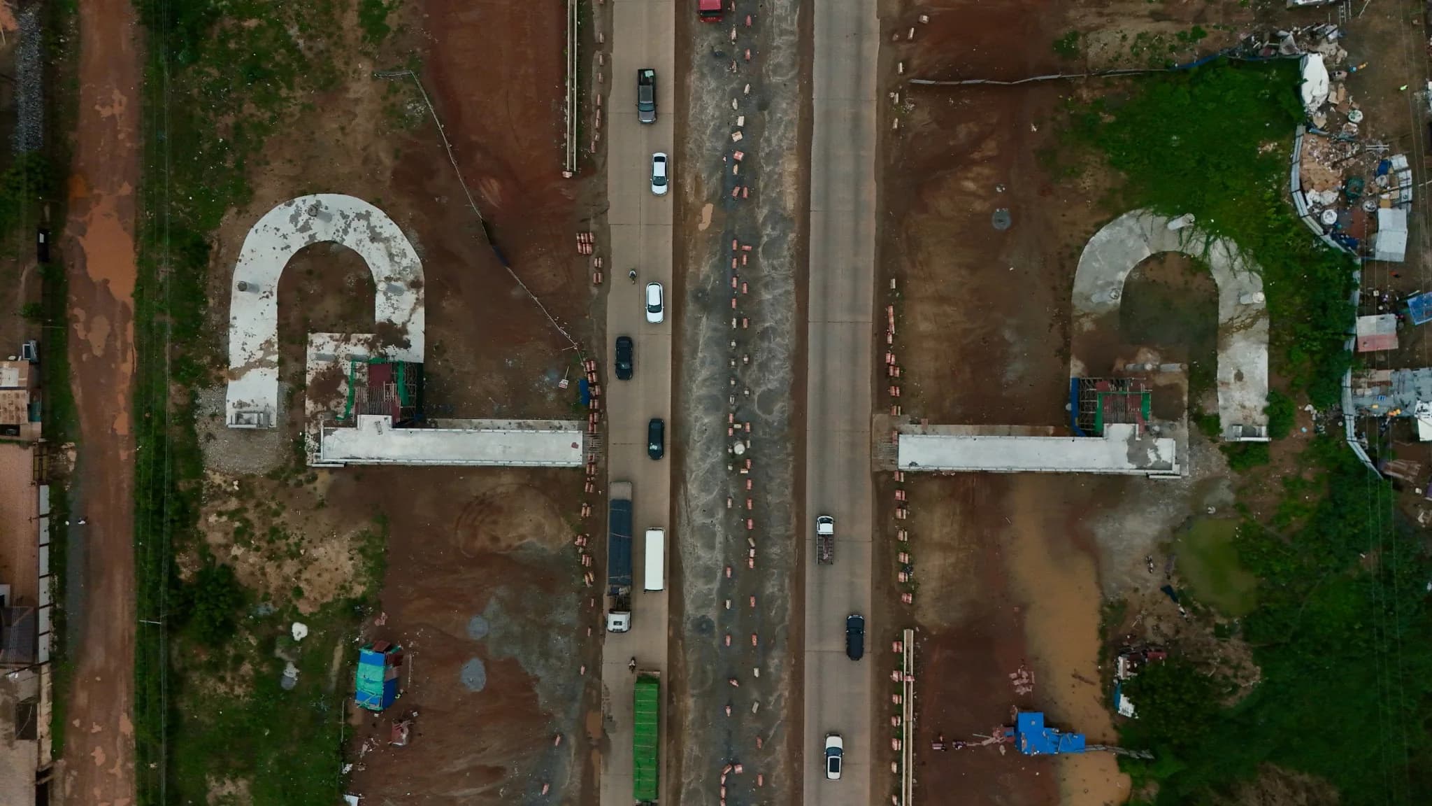 Overhead aerial view of the corridor flanked by U-shaped reinforced-concrete ramp structures, with traffic on the central carriageway