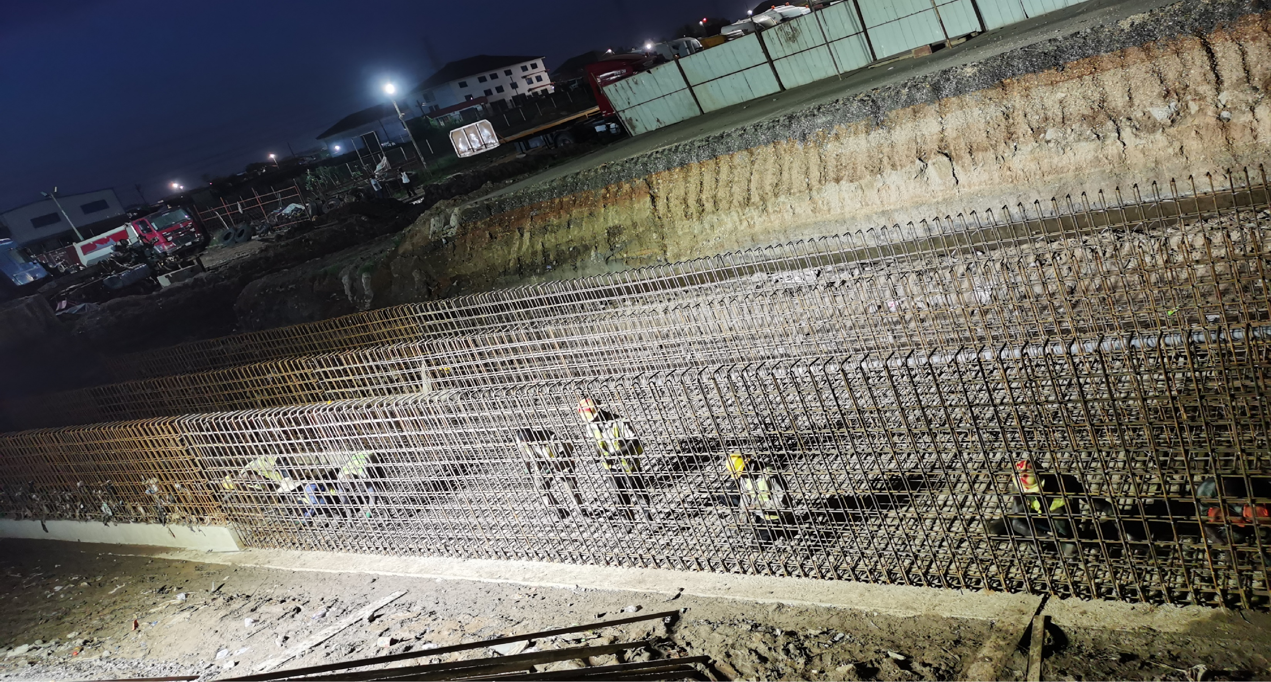 Night-time view of a long reinforcement cage for a retaining wall along an excavated section of the corridor