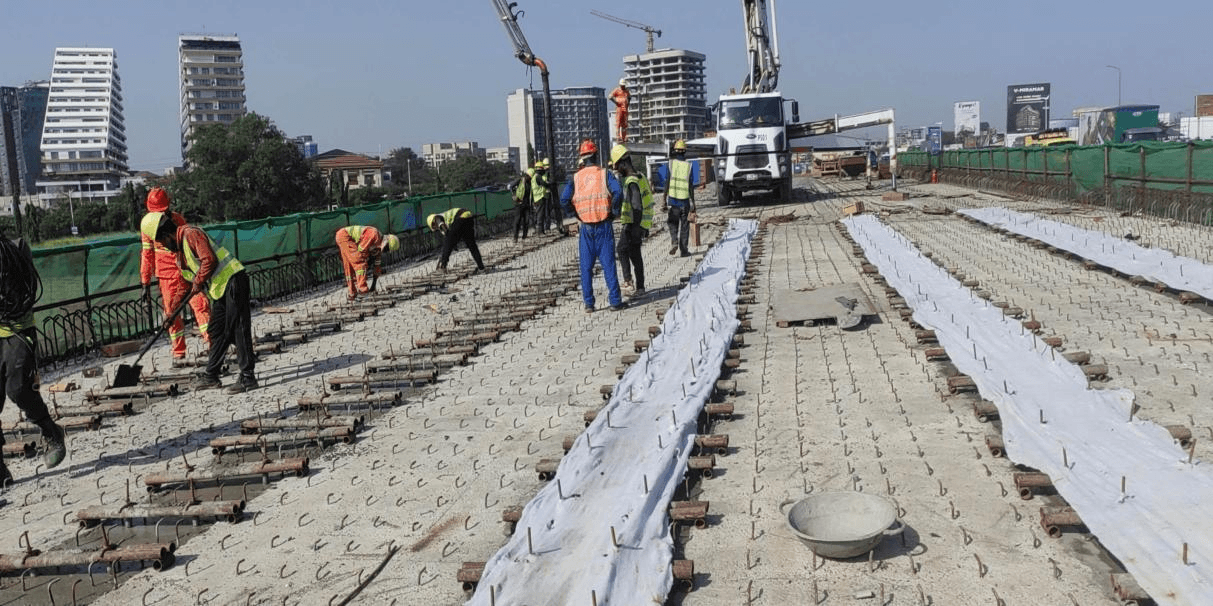 Workers placing deck reinforcement on a bridge deck as a concrete pump delivers concrete