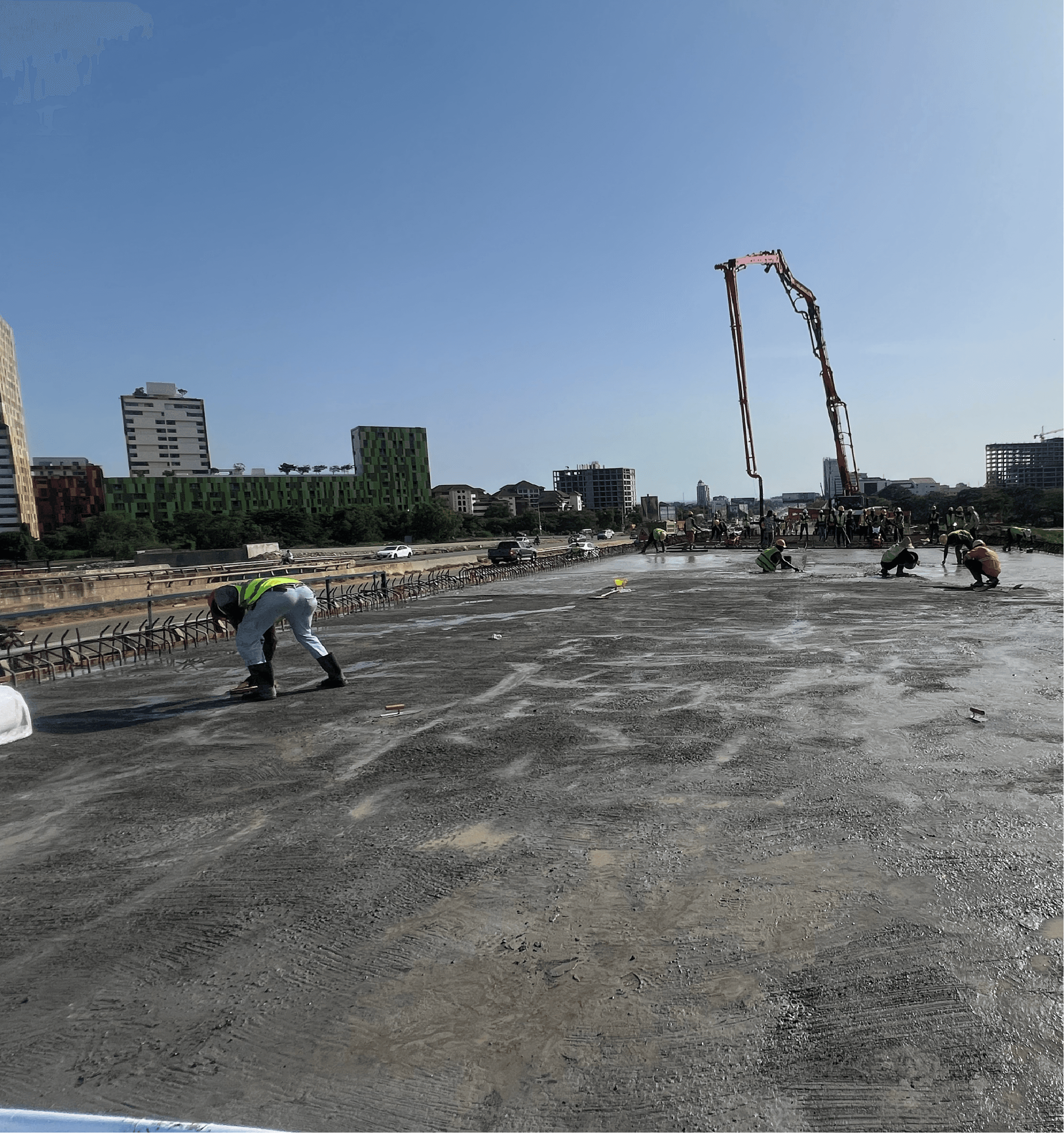 Work crew finishing a freshly poured concrete deck slab as a concrete pump boom reaches across it