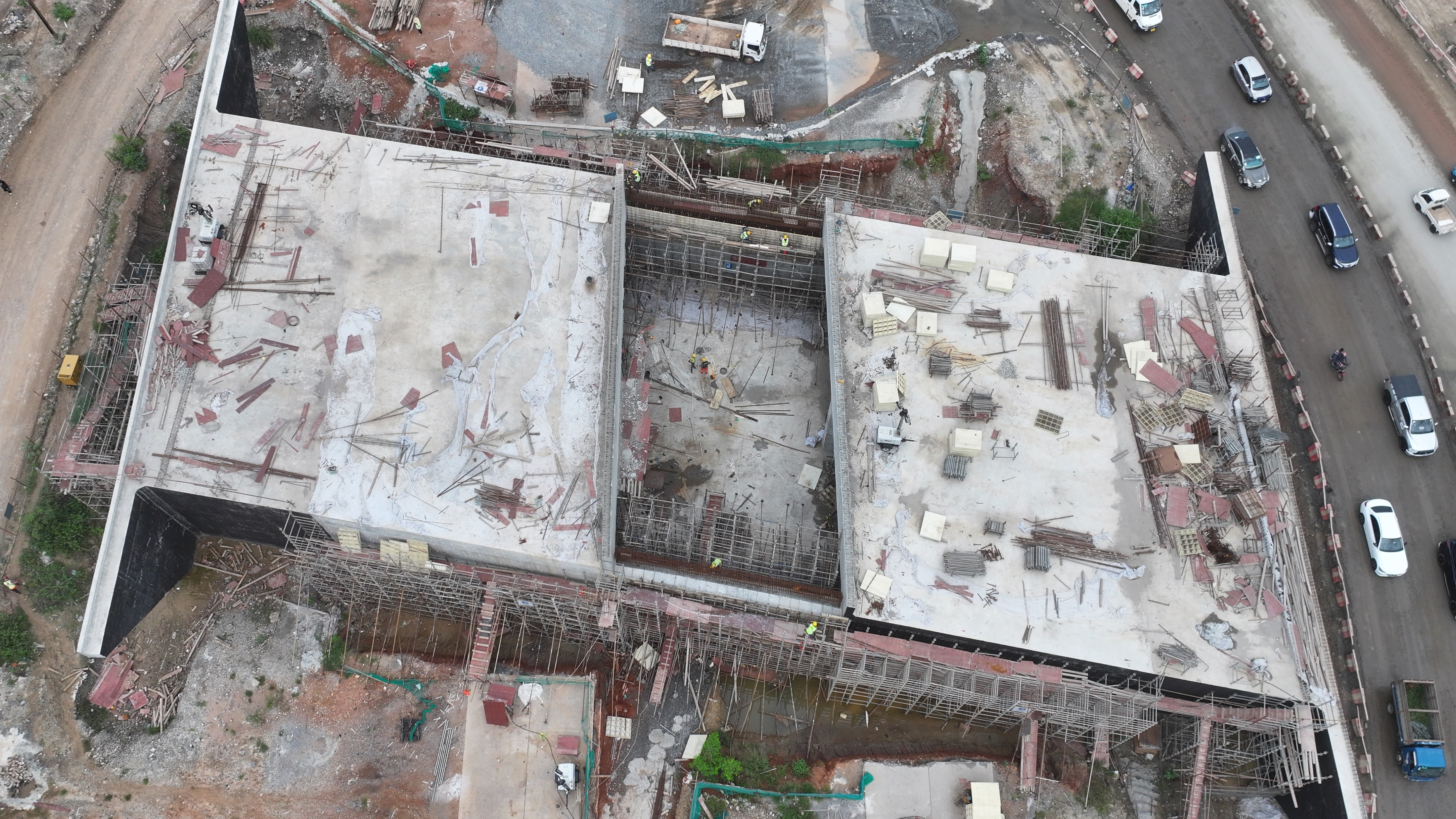 Aerial view of a large reinforced-concrete underpass structure under construction beside a live road