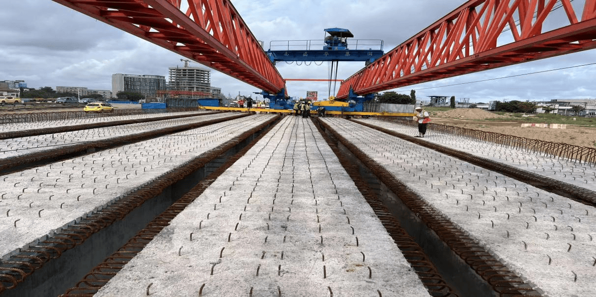 A launching gantry positioning precast T-beams over a bridge span, with reinforcement projecting from the beams