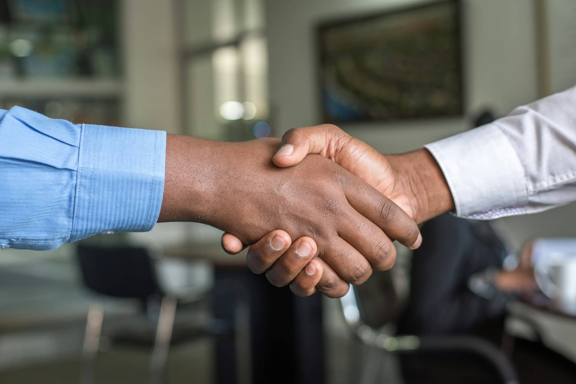 A close-up of two people shaking hands in an office, one in a blue shirt and one in a pale grey shirt